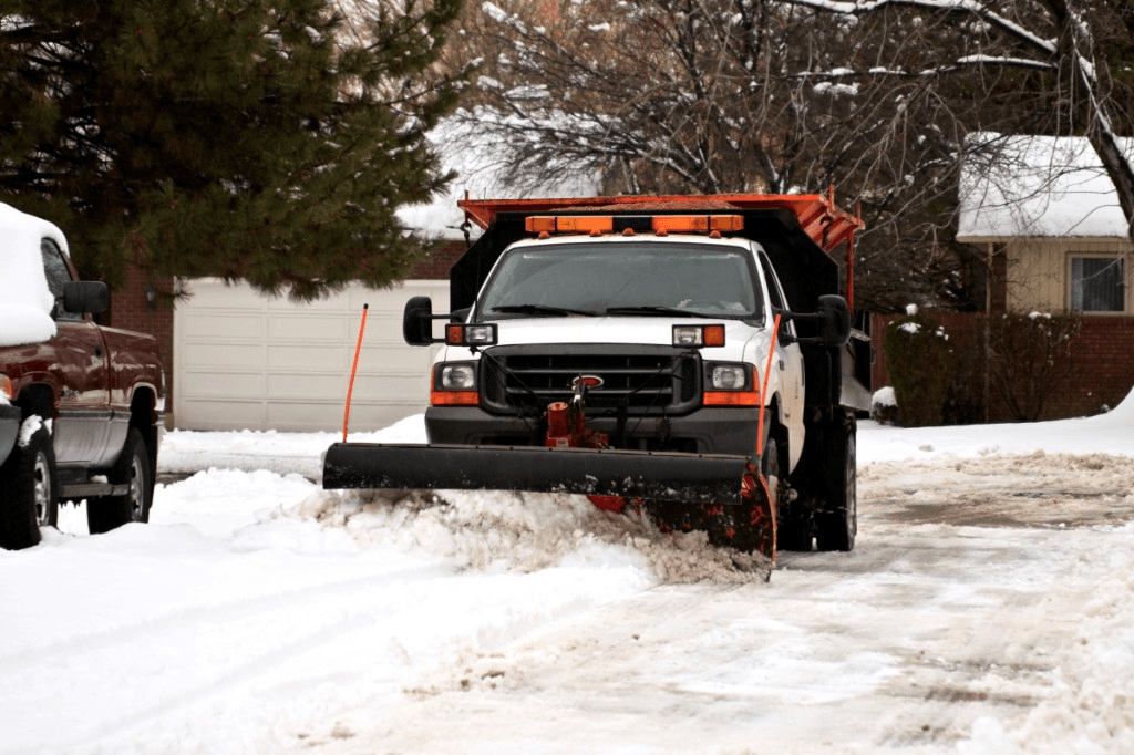 White pickup truck with snow plow and salt spreader clearing slush from a residential street